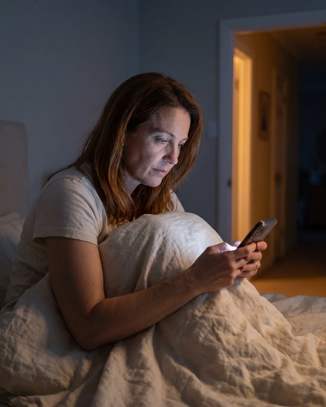 A woman sitting up in bed at 2am, lit by her phone